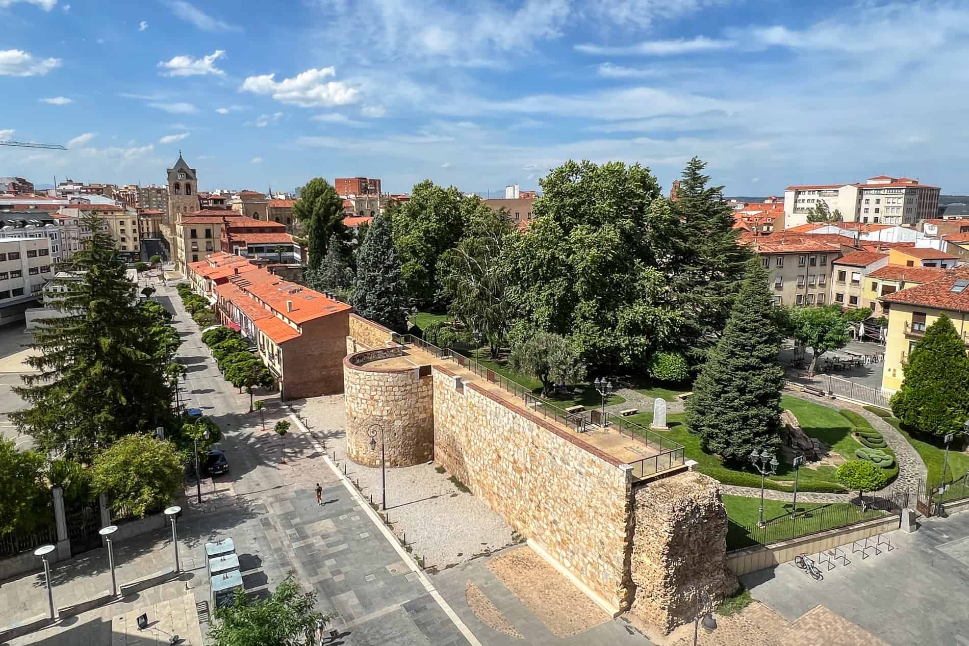Vistas elevadas de las murallas romanas de León, España, entre una calle principal y un parque lleno de árboles. 