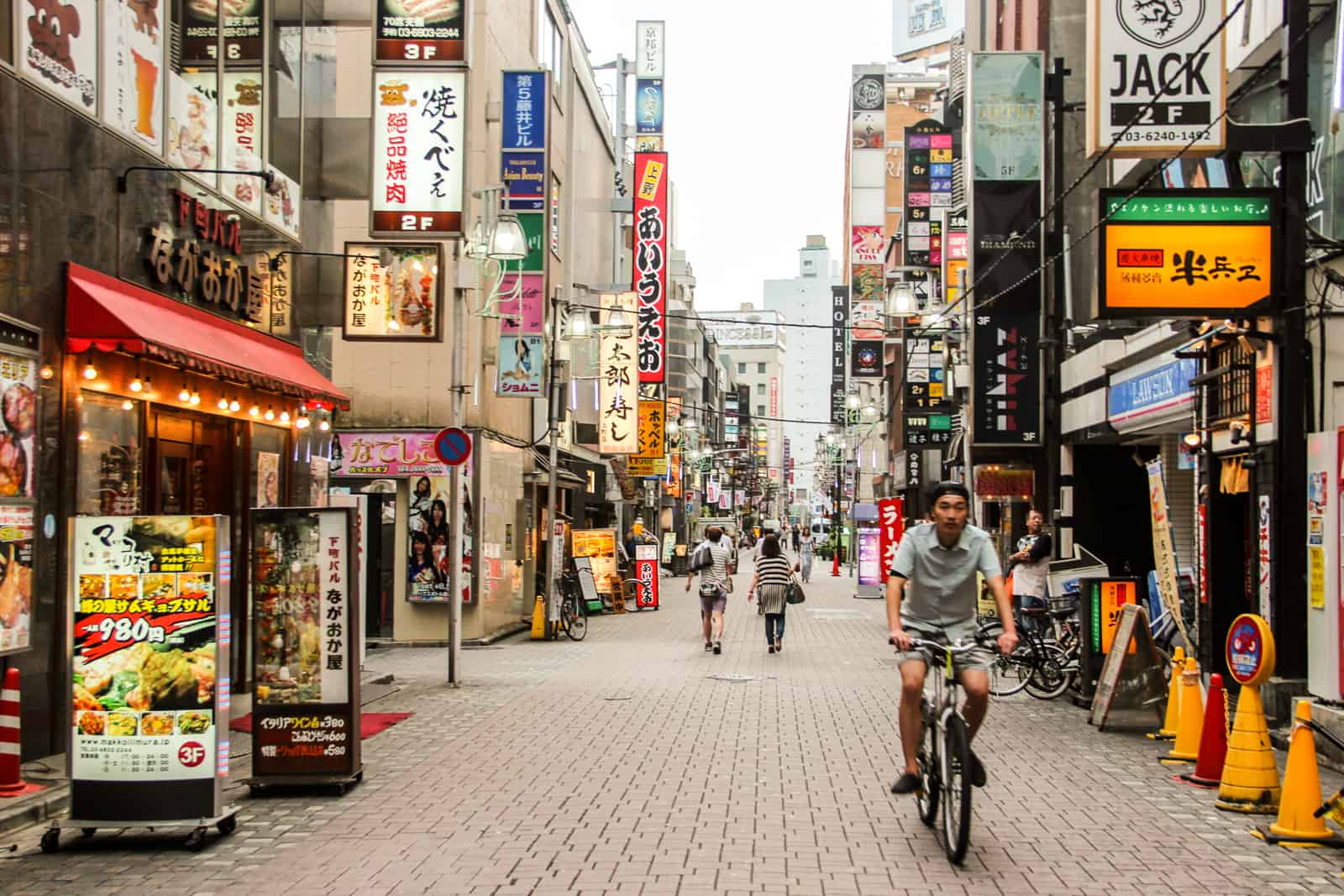 Un hombre va en bicicleta por una calle de Japón con luces de neón y publicidad. 
