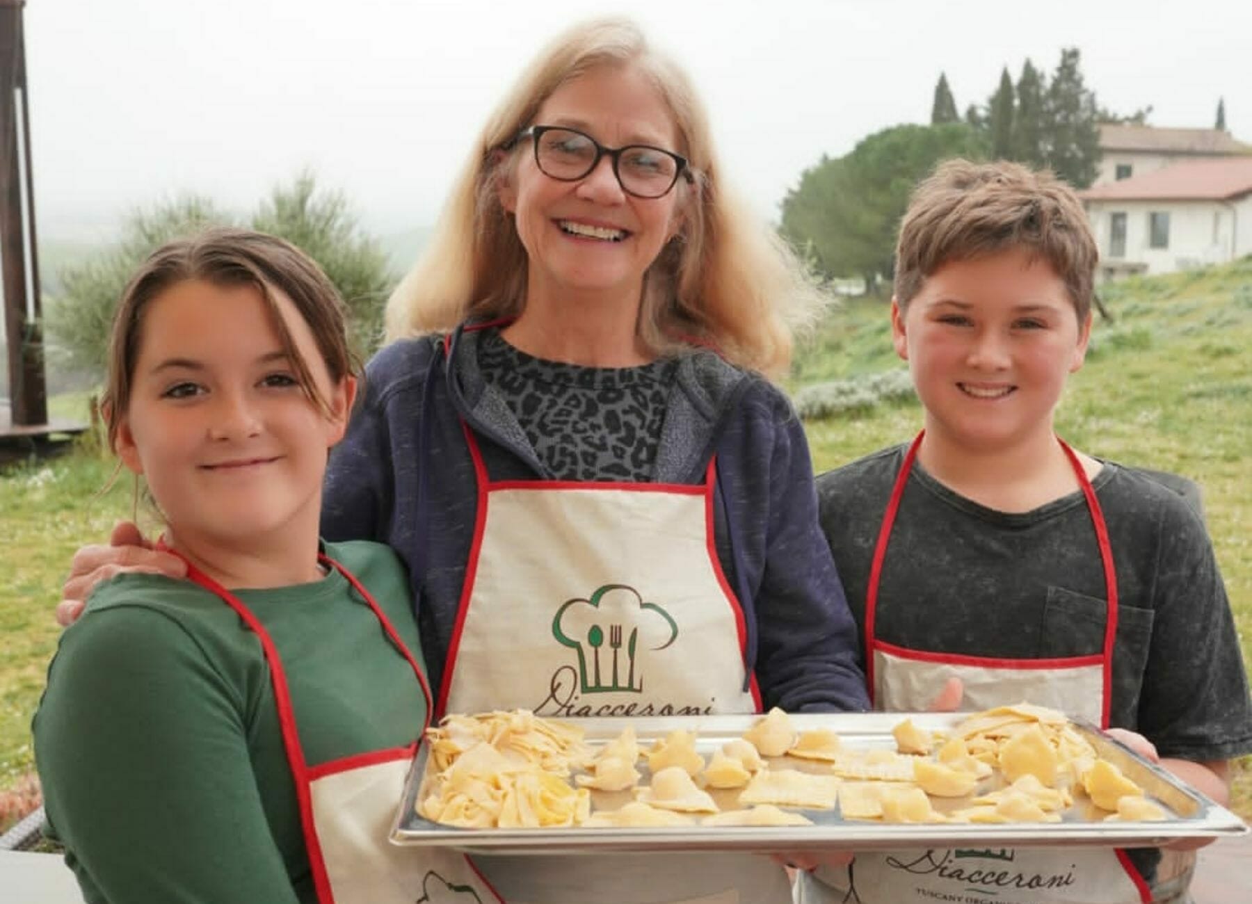 Niños sonrientes y un adulto sosteniendo una bandeja de pasta que hicieron, Cosas que hacer en la Toscana.