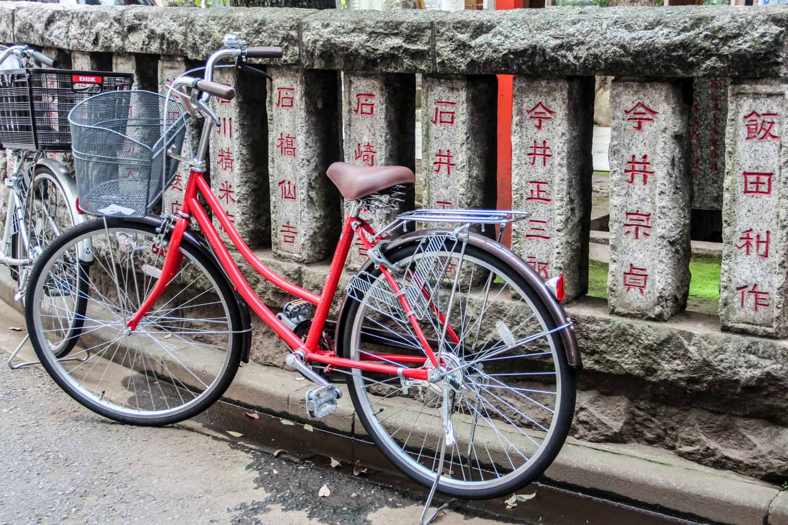 Una bicicleta roja frente a un muro de piedra inscrito con un texto rojo en japonés. 