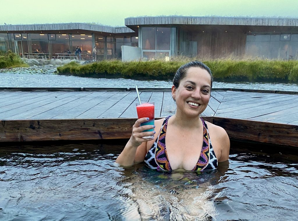 Kate sonríe y sostiene un granizado rojo y azul brillante mientras está sentada en una piscina caliente.
