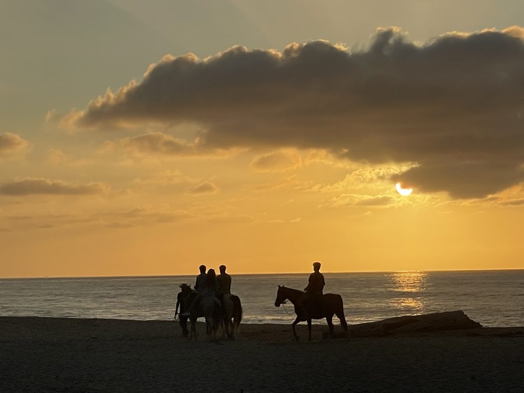 Tres personas montando a caballo en la playa al atardecer.