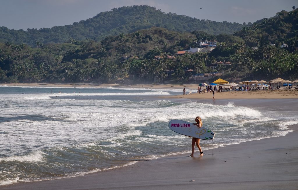 Una mujer sosteniendo una tabla de surf y caminando hacia el océano.