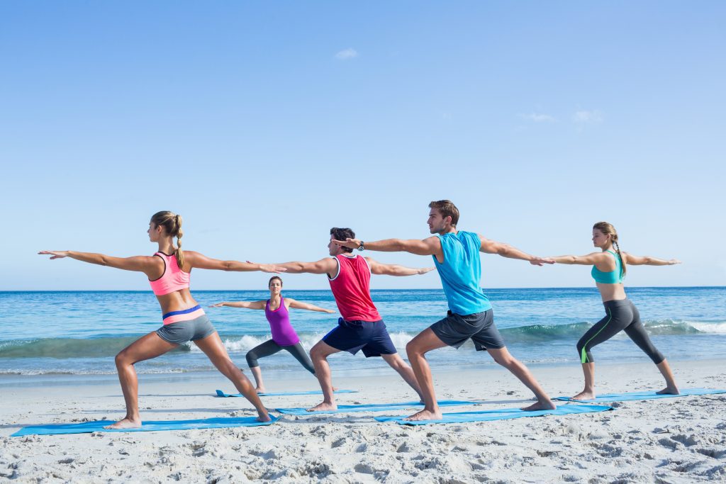 Cinco personas haciendo yoga en la playa en un día soleado.