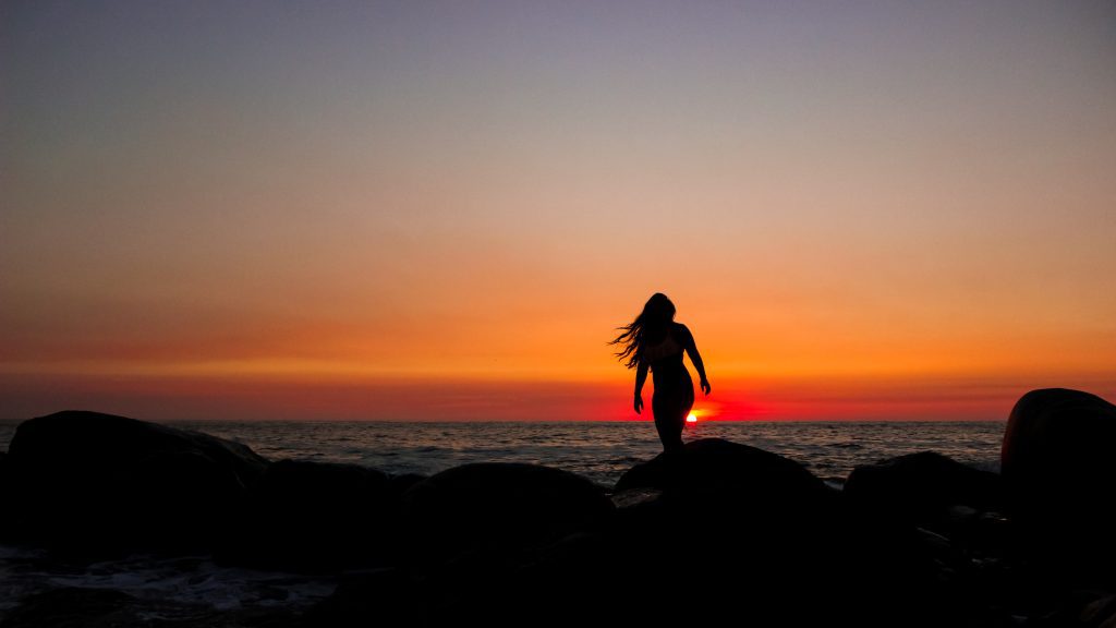 Una mujer mirando un atardecer rojo brillante en la playa.