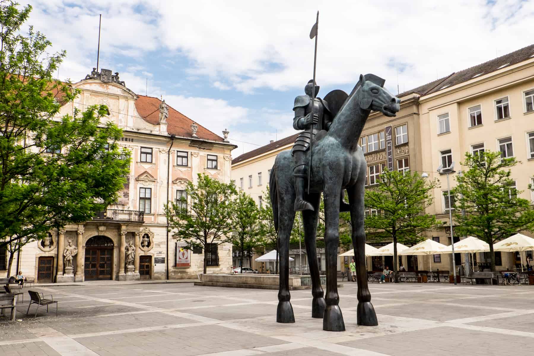 A estatua de un hombre sobre un caballo con patas tipo jirafa, en una plaza de edificios dorados en Brno, República Checa.