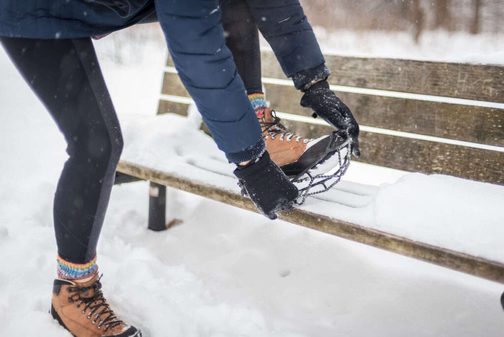 Mujer poniéndose microspikes durante el invierno bota de senderismo en un banco nevado