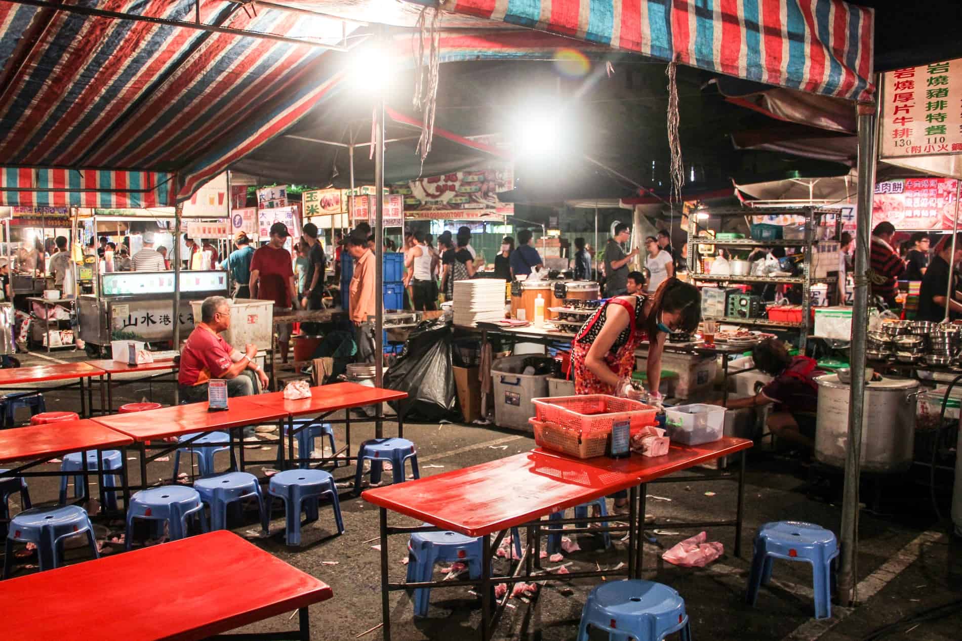Mesas rojas y sillas azules detrás de un vendedor de alimentos en uno de los mercados nocturnos de Tainan. 